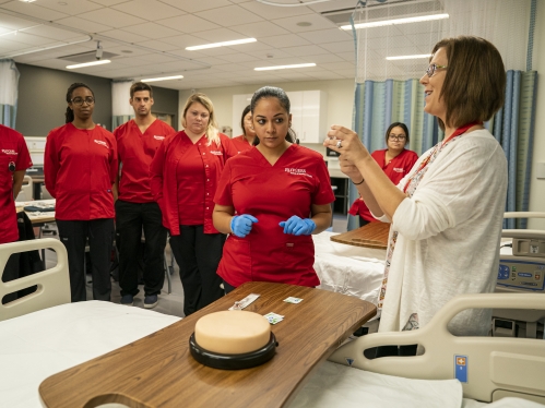 a female nurse demonstrating a procedure to mixed gender nursing students in a hospital room