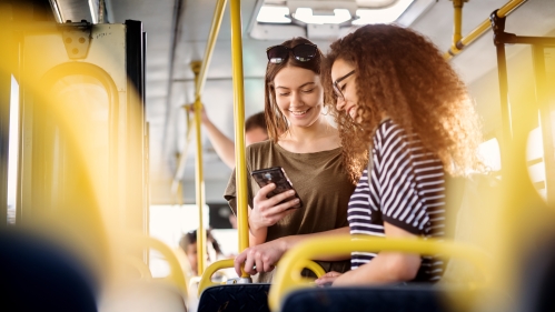 two women smiling and looking at phone on bus