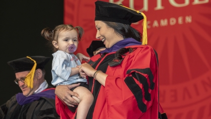 Law graduate about to receive diploma on stage carries small child with her